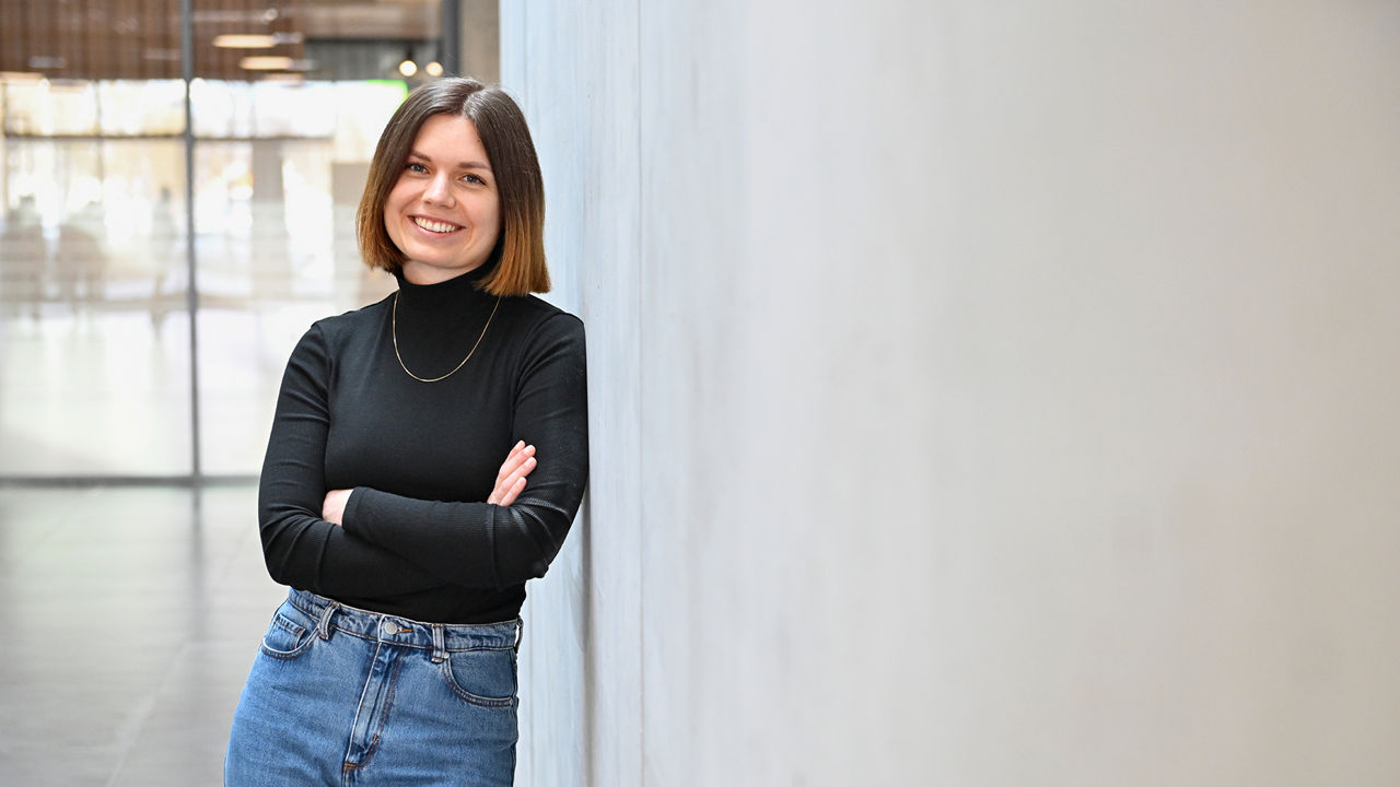 Lisa, Product Designerin SDC, lächelt in die Kamera und lehnt sich an eine Wand